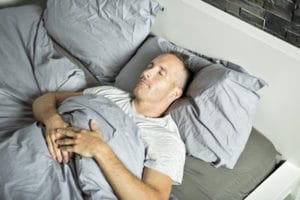 Мужчина лежит в кровати на спине