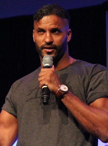 Ricky Whittle on stage with a microphone speaking to an audience with his new hair transplant