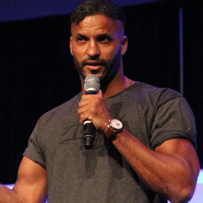 Ricky Whittle on stage with a microphone speaking to an audience with his new hair transplant