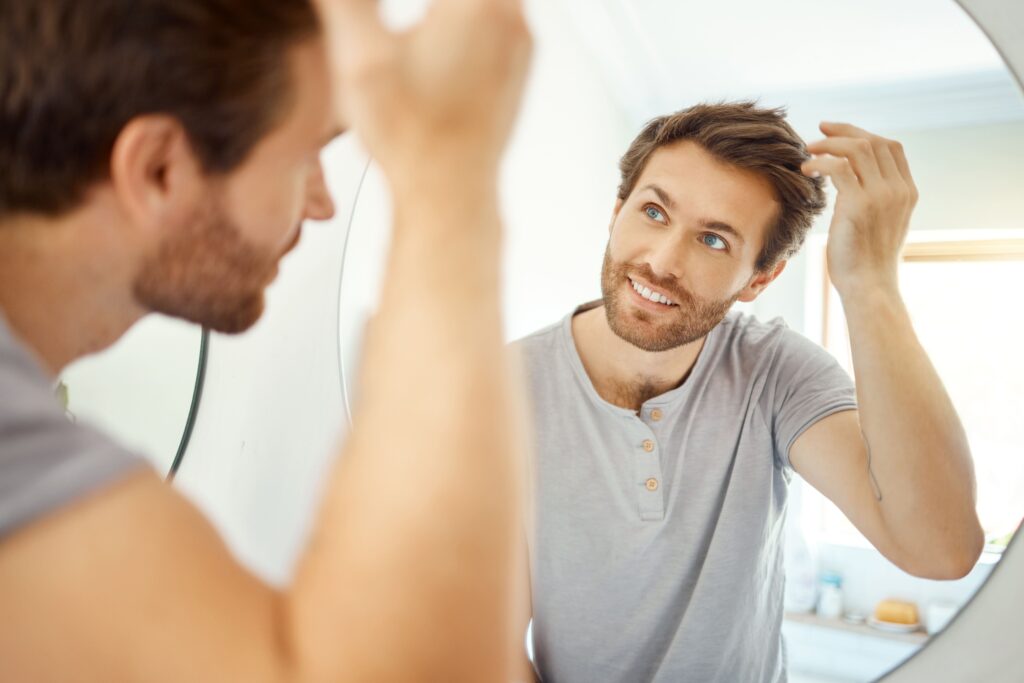 Happy man looking in a mirror at his hair growth after he stopped smoking