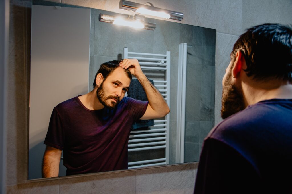 A young man looks at himself in the mirror and inspects his premature receding hairline.
