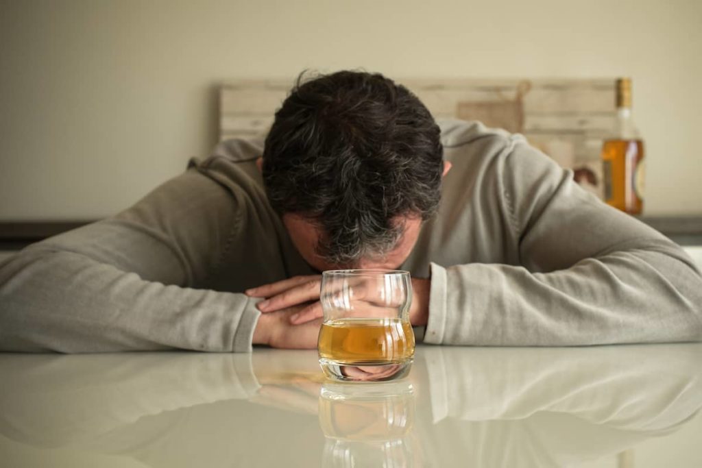 Czy alkohol powoduje wypadanie włosów? Mężczyzna leżący z głową na stole za szklanką whisky