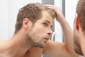 Mężczyzna patrzący na włosy w lustrze i zadający sobie pytanie, jaki jest najlepszy wiek na przeszczep włosów