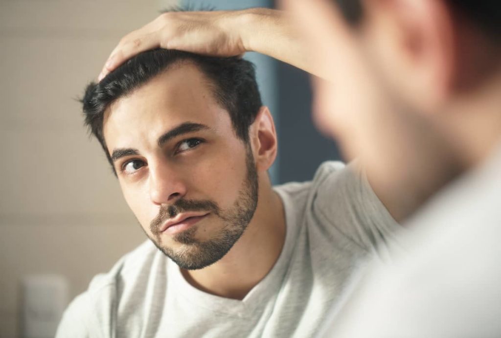 Man looking at receding hair in mirror