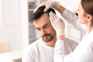 Médecin examinant les cheveux d'un jeune homme dans une clinique, gros plan