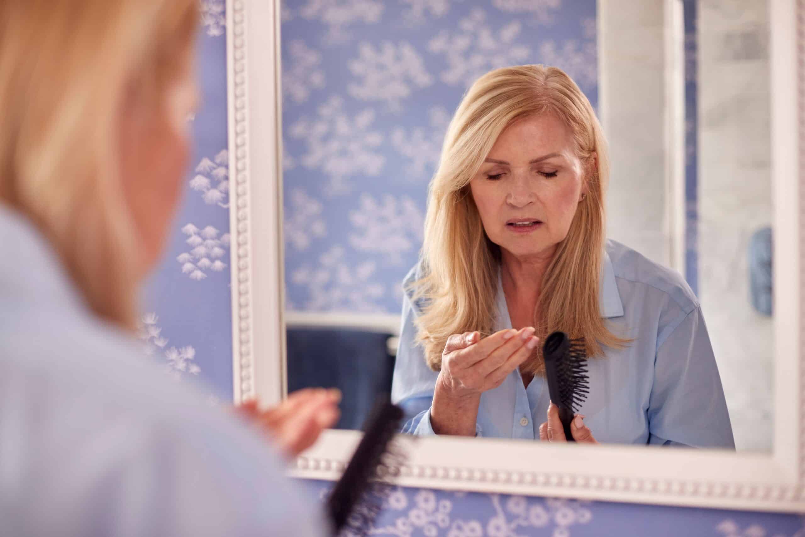 Menopausal Mature Woman Suffering Hair Loss Brushing Hair In Mirror At Home