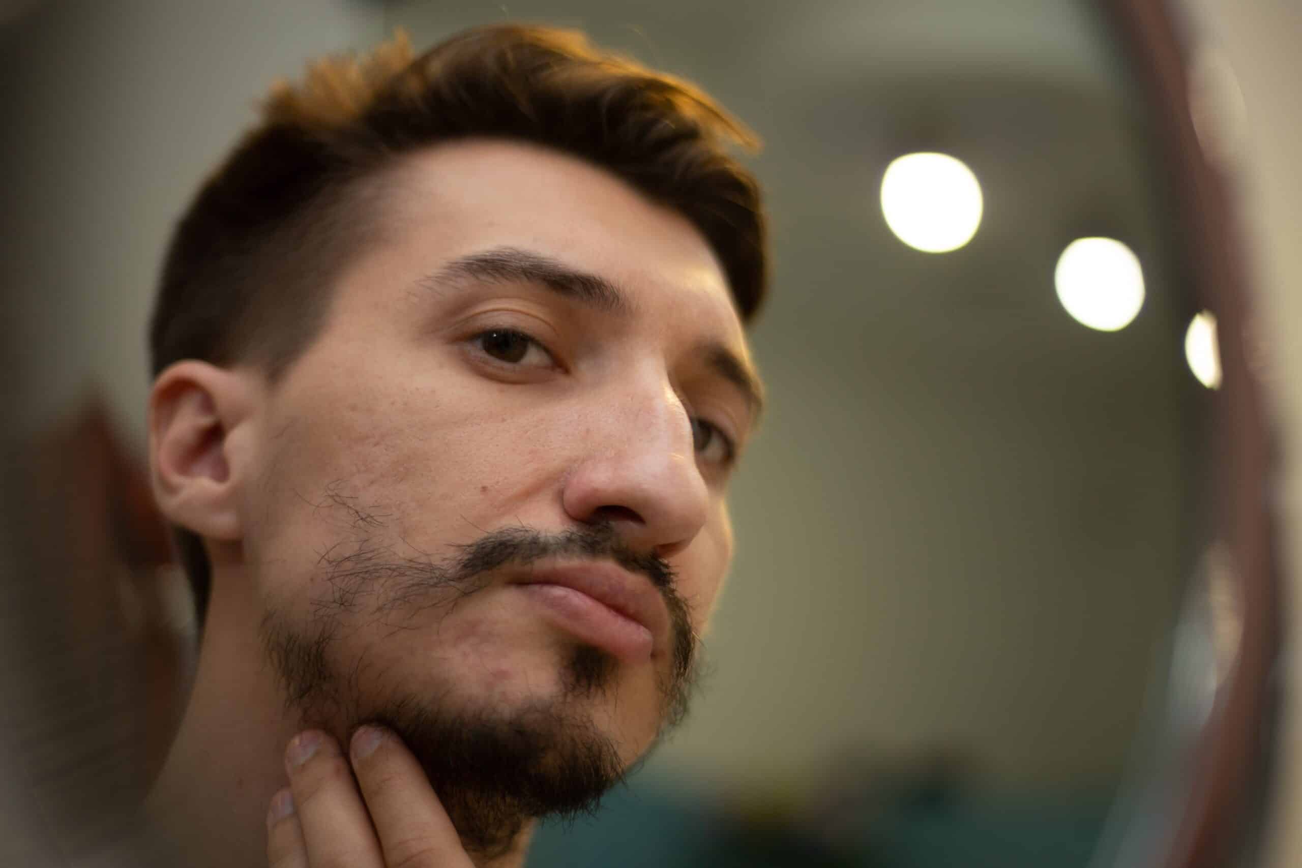 Man worried about his patchy beard growth, looking in a mirror