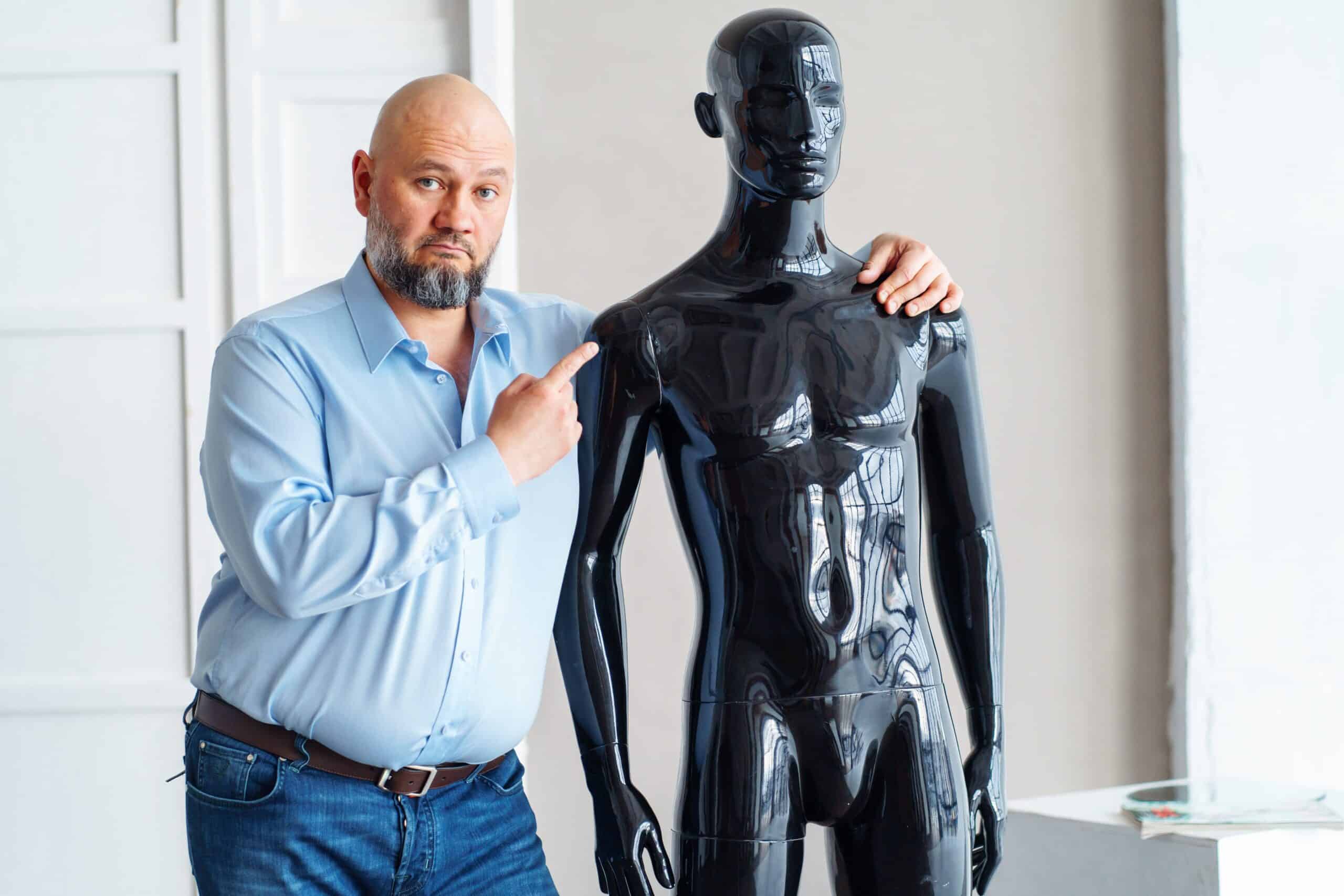 Bald man standing next to a plastic model. Bald men are good candidates for artificial hair transplants