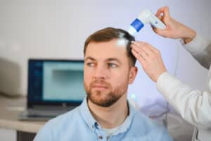 Una doctora observa el cuero cabelludo de un hombre con un dermatoscopio.