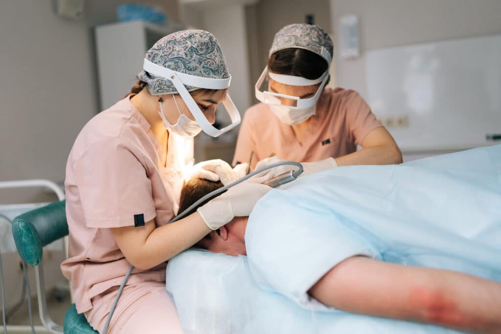 Dos doctoras recogen folículos pilosos de la zona donante de un paciente masculino para un trasplante capilar.