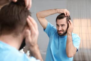 Un hombre se pregunta qué hacer después de un injerto capilar mientras se mira al espejo