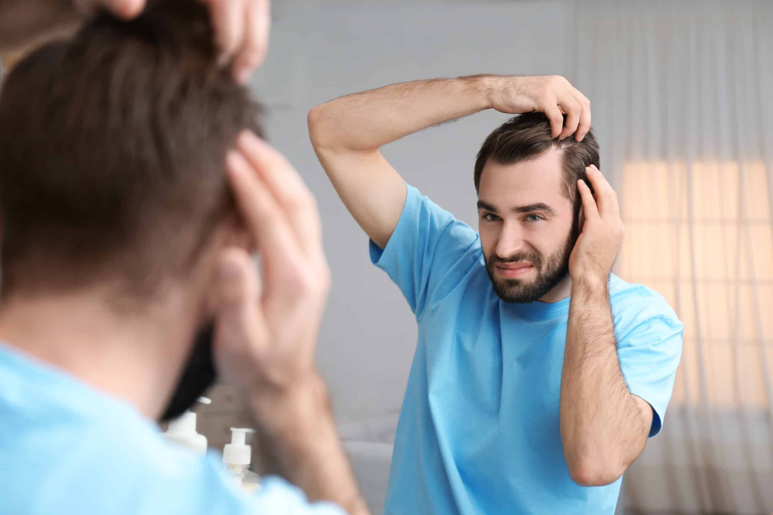 Un hombre se pregunta qué hacer después de un injerto capilar mientras se mira al espejo