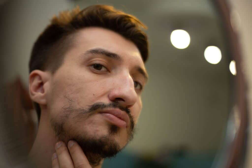 Photo d’un homme remarquant une perte de poils de barbe devant le miroir