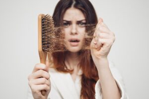 Femme inquiète qui montre une brosse pleine de cheveux à cause de l’alcool et perte de cheveux