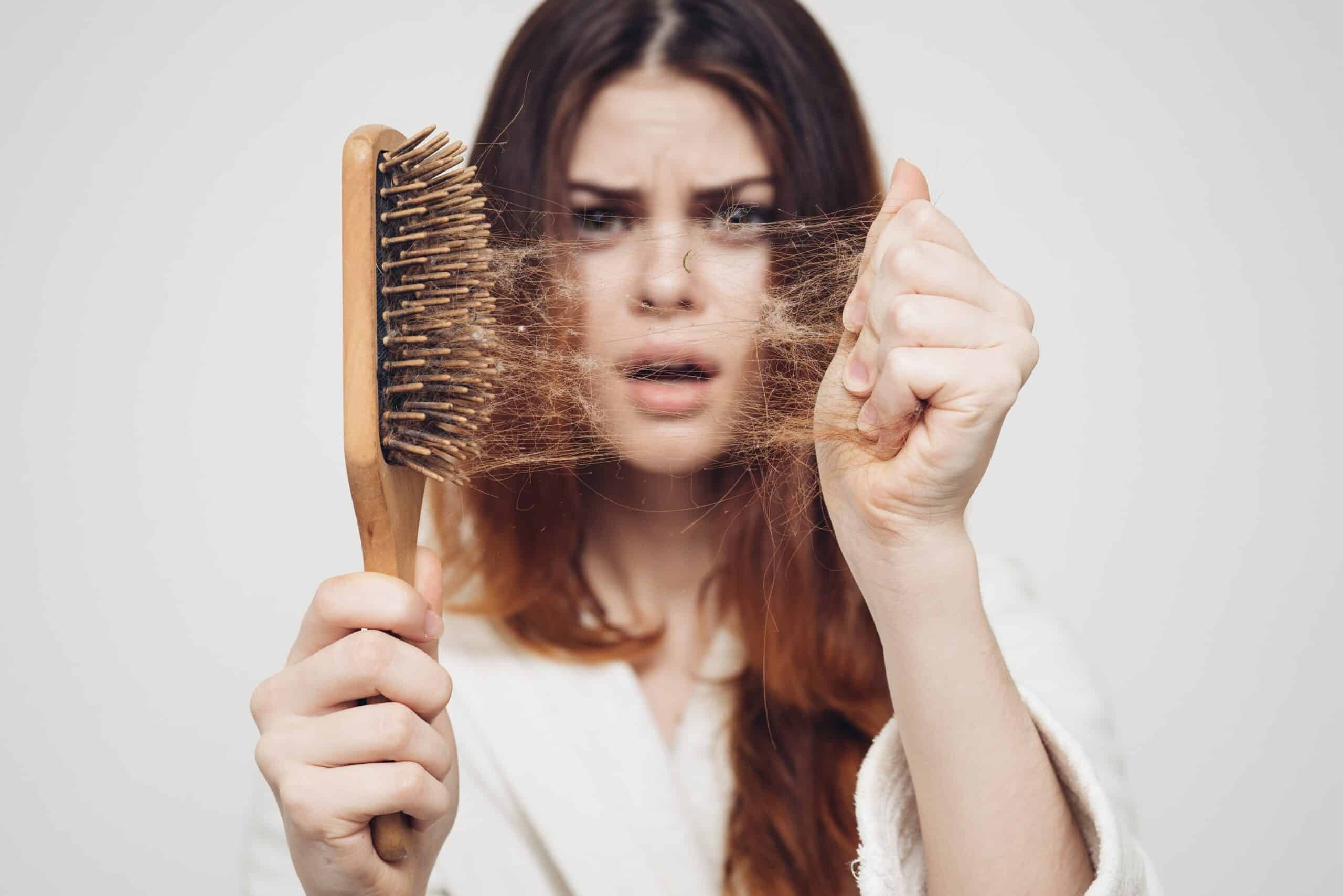 Femme inquiète qui montre une brosse pleine de cheveux à cause de l’alcool et perte de cheveux