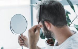 Uomo si guarda allo specchio per capire quando fare il trapianto di capelli