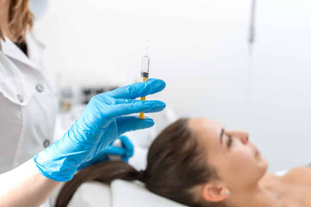 L'estetista tiene in mano una siringa con un'iniezione per la rigenerazione dei capelli