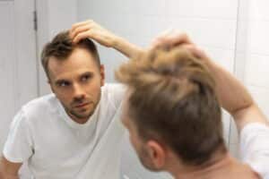Un homme regarde ses cheveux dans le miroir de sa salle de bain et s'inquiète de sa calvitie.