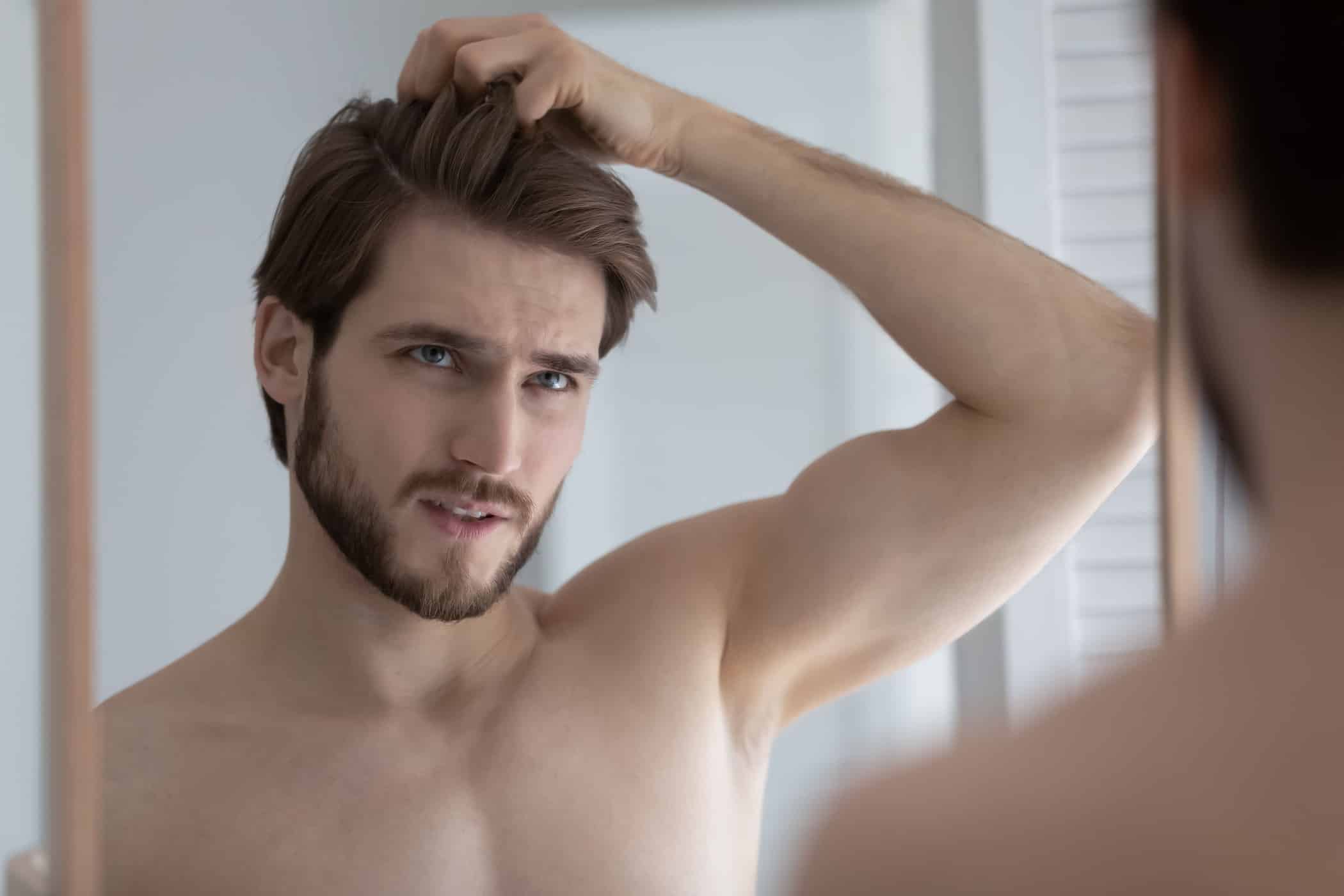 Uomo si guarda allo specchio frustrato dal ciuffo ribelle