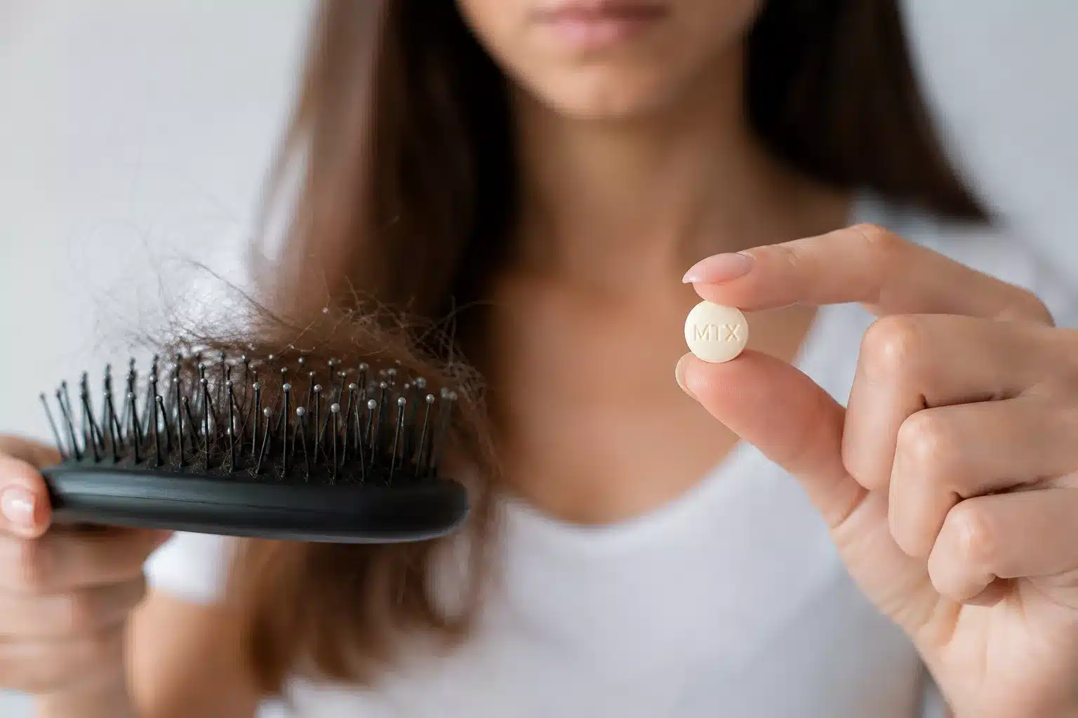 Frau hält eine Haarbürste mit ausgefallenen Haaren und eine unbeschriftete Tablette als Symbol für möglichen Haarausfall im Zusammenhang mit Medikamenten.