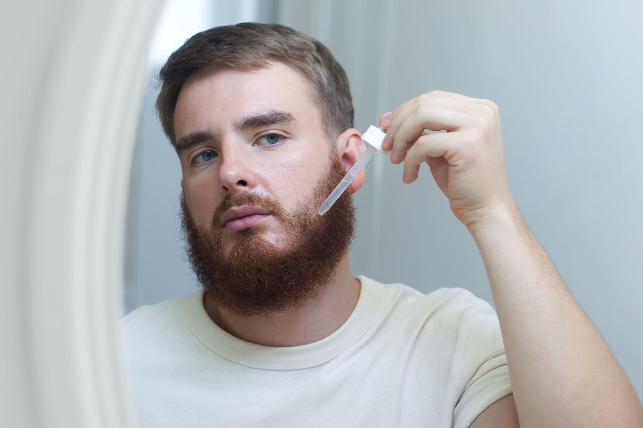 Minoxidil barba: uomo applica minoxidil sulle guance con contagocce