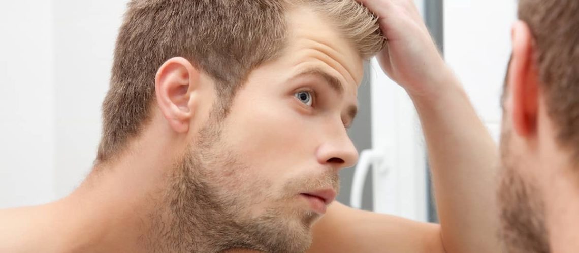 Man looking at hair in the mirror asking himself what the best age for a hair transplant is