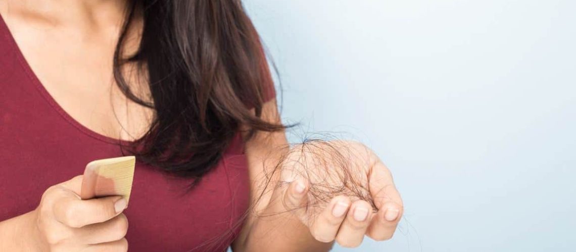 Женщина с расческой в руках на которой выпавшие волосы
